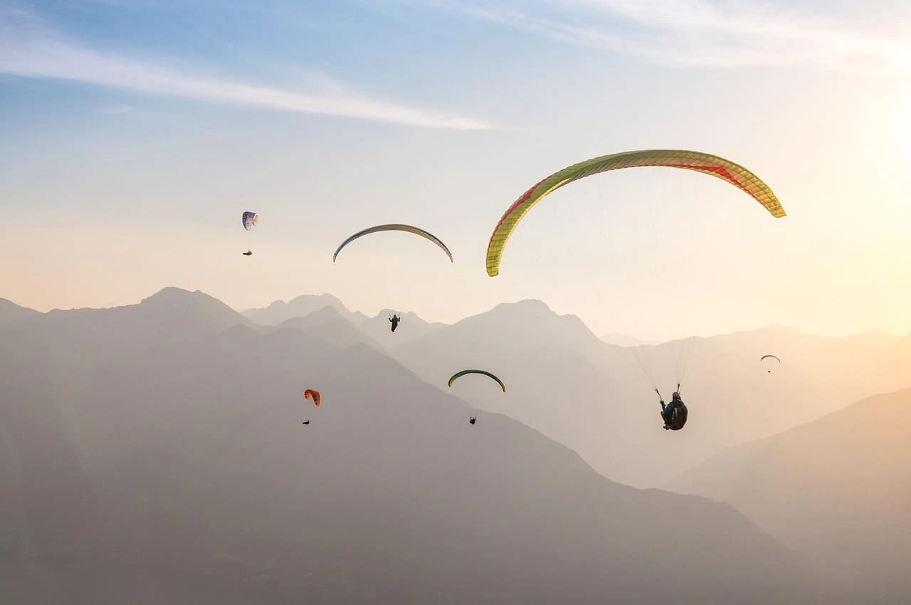 Tandem paragliders flying over the Almaty mountains at sunset
