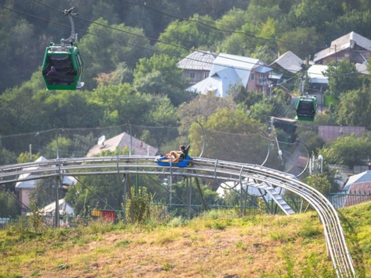 Kok Tobe alpine coaster ride with cable cars passing above green hills in Almaty