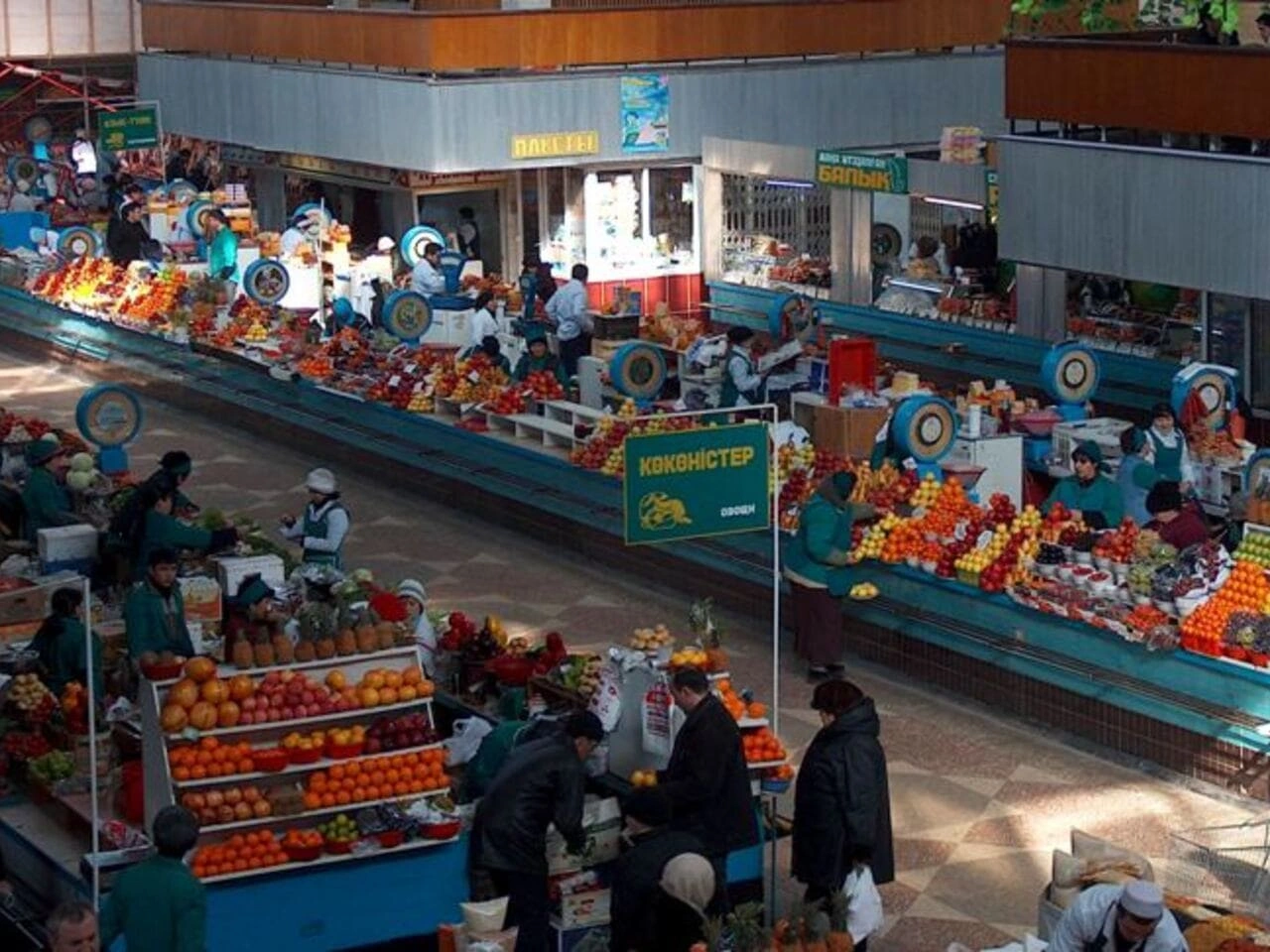 Colorful fruit and vegetable rows at Almaty’s Green Bazaar with shoppers and vendors.