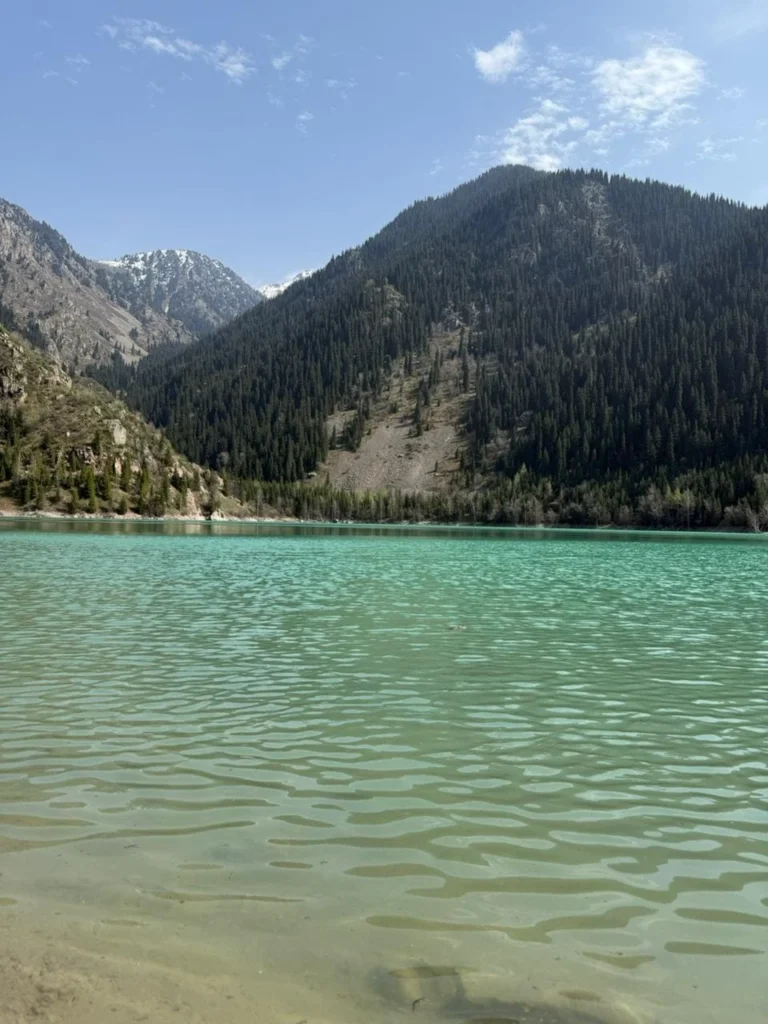 Beautiful panoramic view of Issyk Lake reflecting the Tian Shan mountains under a bright blue sky.