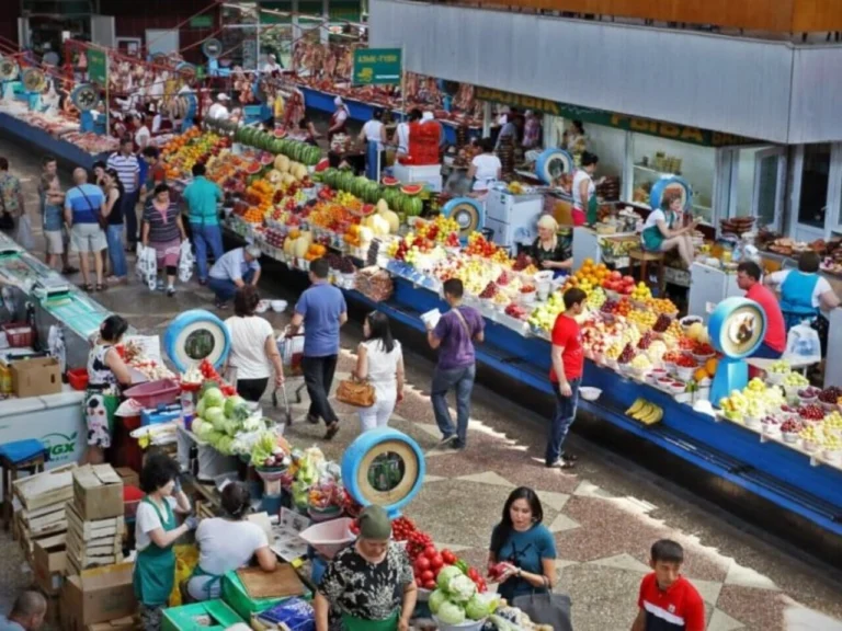 Indoor fruit and vegetable stalls at Green Bazaar in Almaty with visitors walking between rows.