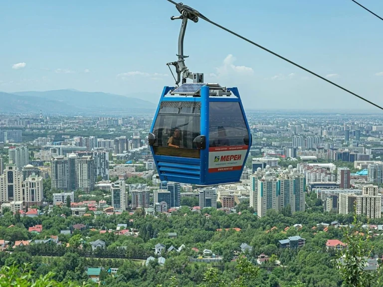 Blue cable car descending from Kok Tobe with panoramic view of Almaty city