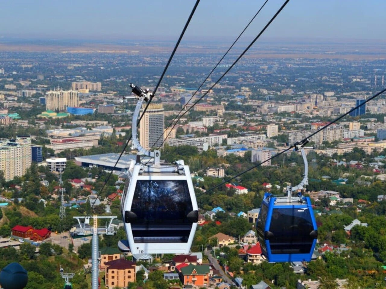 Two cable cars traveling above Almaty with a wide panoramic view of the city