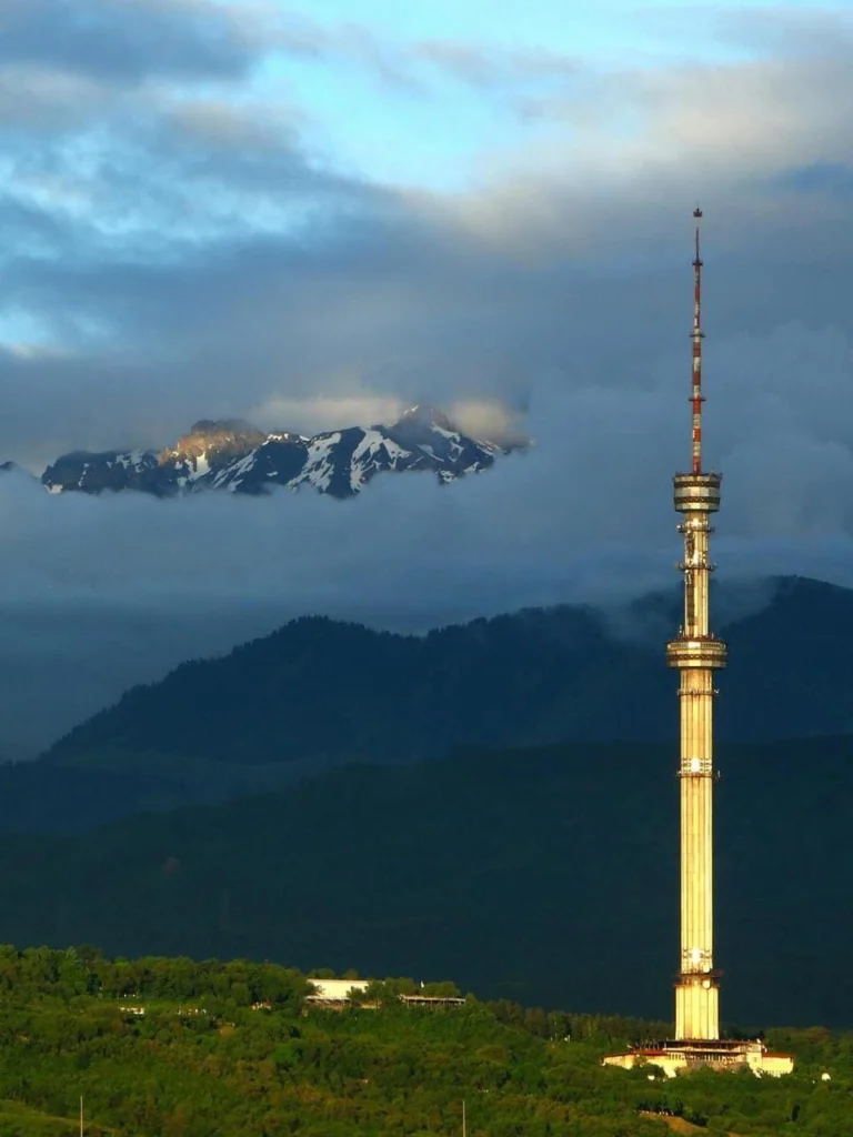 Kok Tobe TV tower rising above green hills and mountain backdrop in Almaty