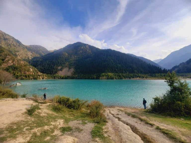 Visitors taking photos at the Issyk Lake viewpoint with snow-capped mountains in the background.