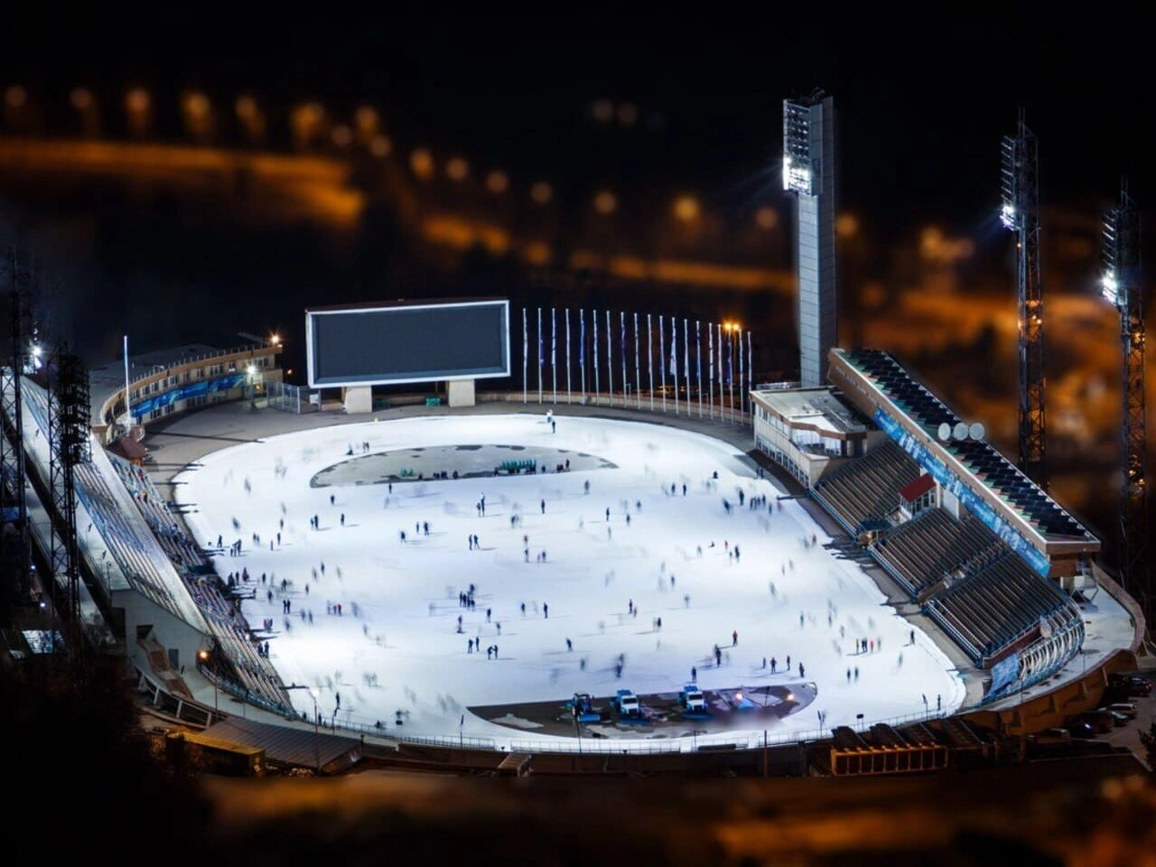 Night aerial view of the Medeo ice rink in Almaty with skaters on the illuminated ice.