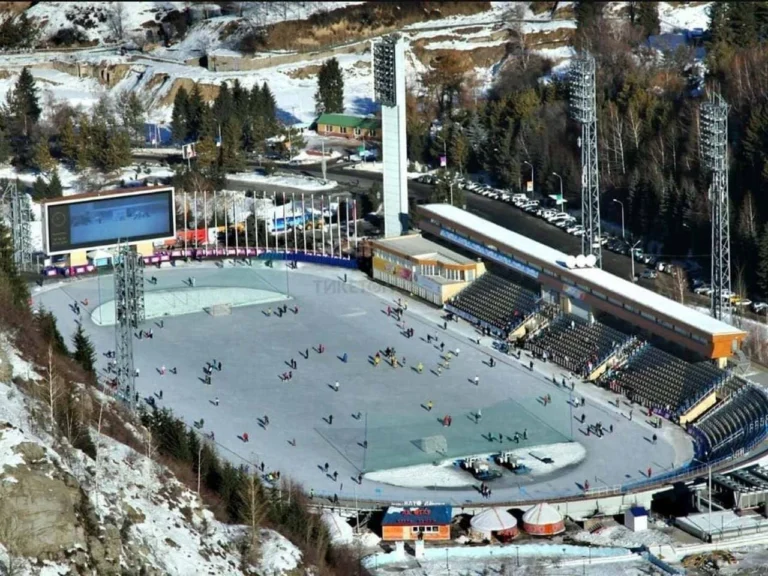 Winter view of the Medeo ice rink with skaters and surrounding snowy mountains.